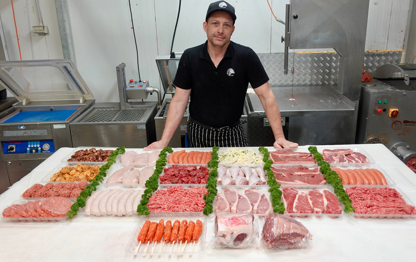 Person standing behind a display of various cuts of meat in a kitchen setting.