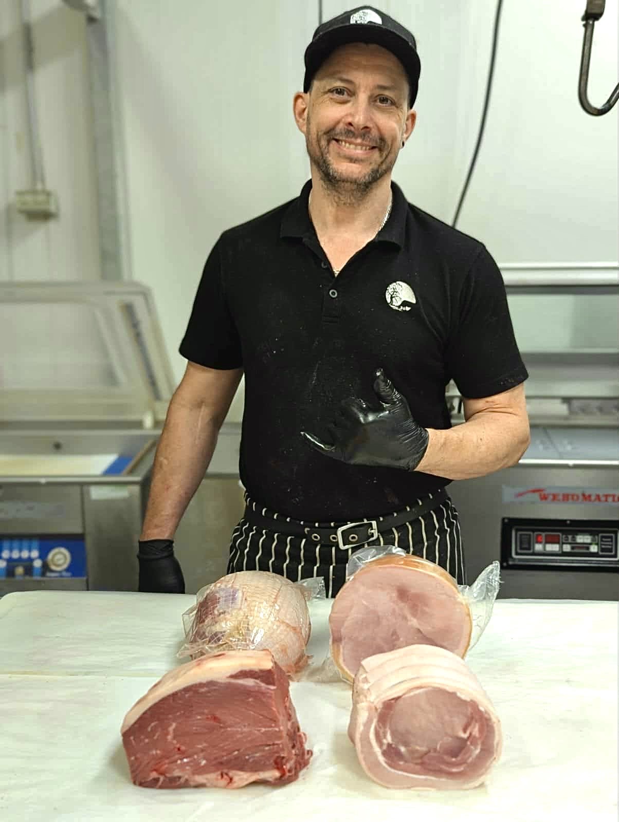 Man in a black shirt and gloves holding a piece of meat in a kitchen setting