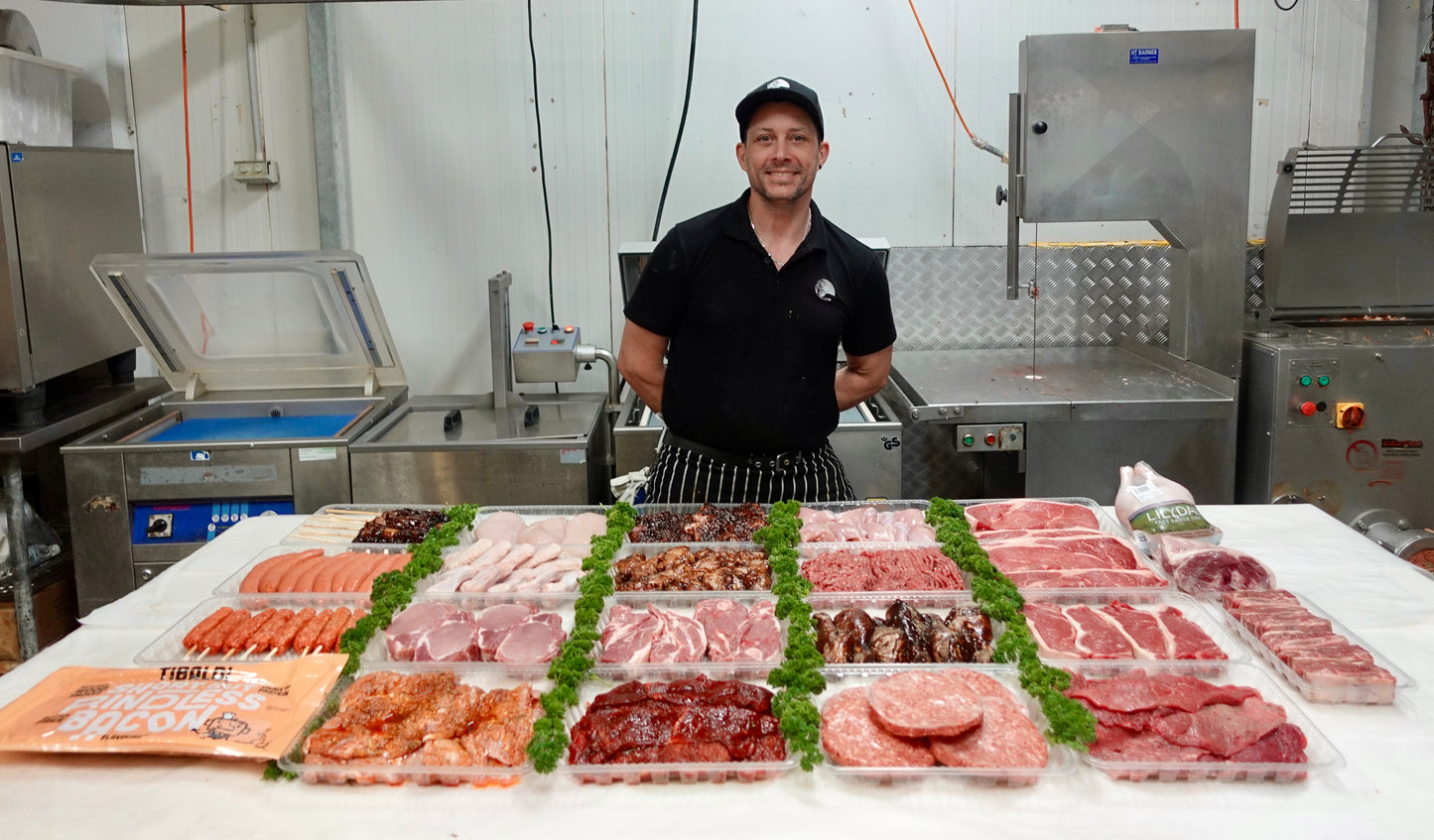 Man standing behind a counter displaying various packaged meats in a kitchen setting.