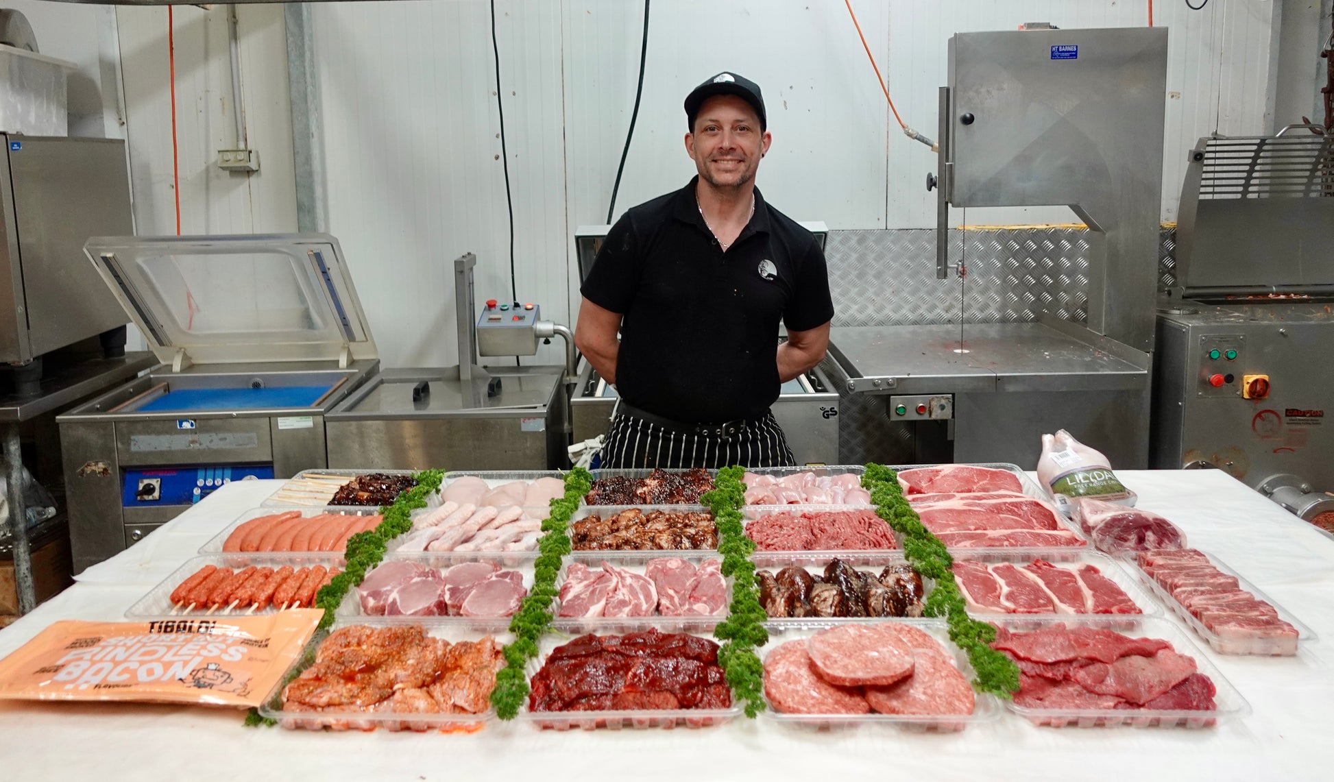 Man standing behind a counter displaying various packaged meats in a kitchen setting.