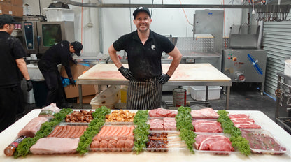 Butcher standing behind a display of raw meat in a kitchen setting