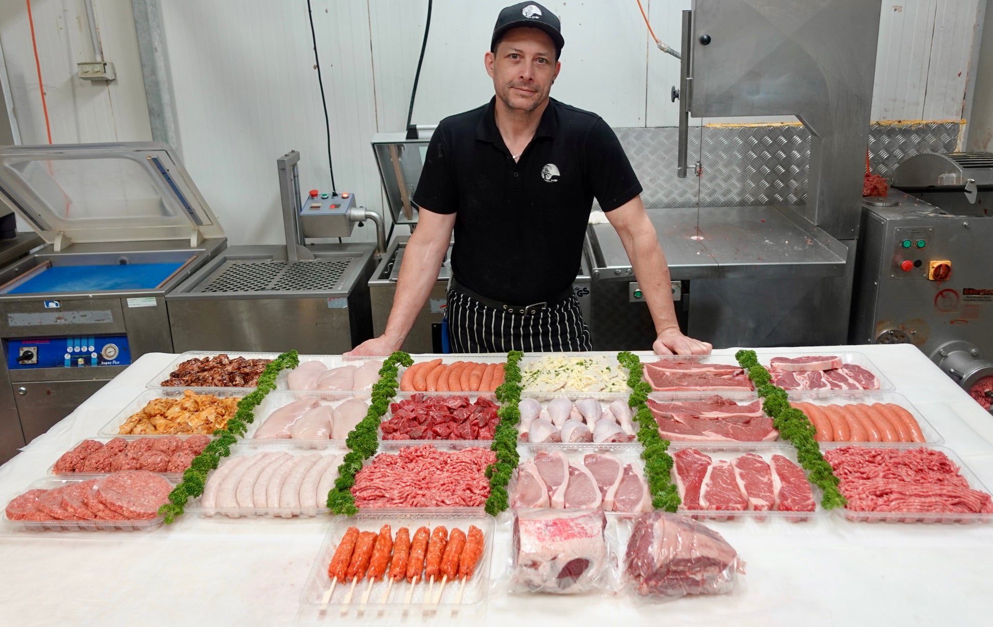 Person standing behind a display of various cuts of meat in a kitchen setting.