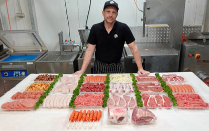 Person standing behind a display of various cuts of meat in a kitchen setting.